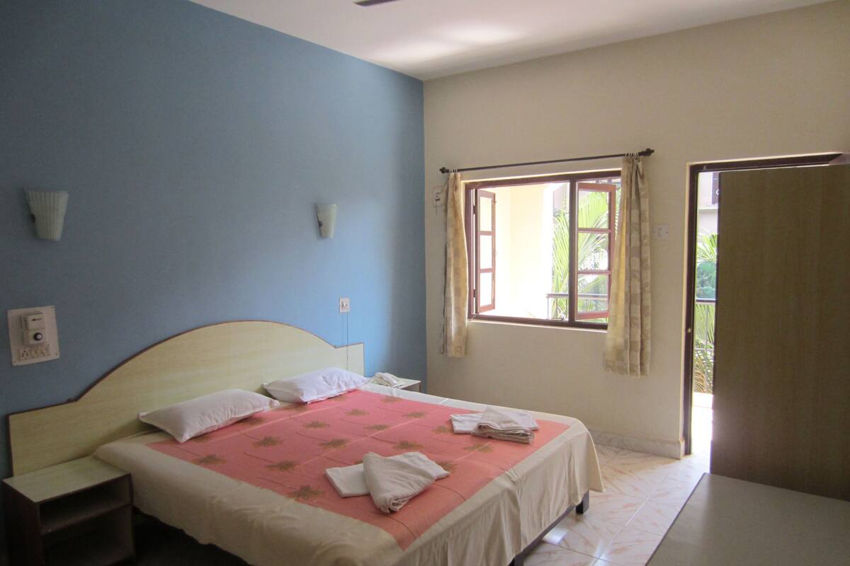 A bedroom with a bed, a nightstand, a ceiling fan, a window with curtains, and a door.