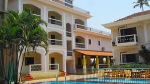 A hotel with a swimming pool, multiple balconies, and outdoor seating. - Riverside Regency Resort (Baga)