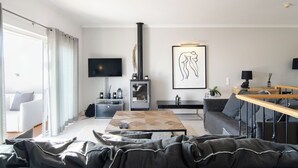 A modern living room with a fireplace, a flat-screen TV, a sofa, a coffee table, and a dining area. - Apartamentos Turísticos The View (Vila do Bispo)