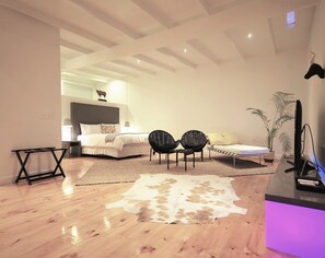 A modern living room with a wooden floor, a large rug, two black chairs, a sofa, a TV, and a ceiling with exposed beams. - DysART Boutique Hotel (Cape Town)