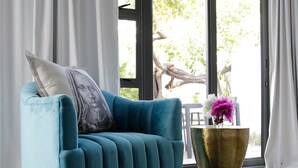 Uma poltrona azul-esverdeada com base dourada, um travesseiro branco e um vaso dourado com flores cor-de-rosa.