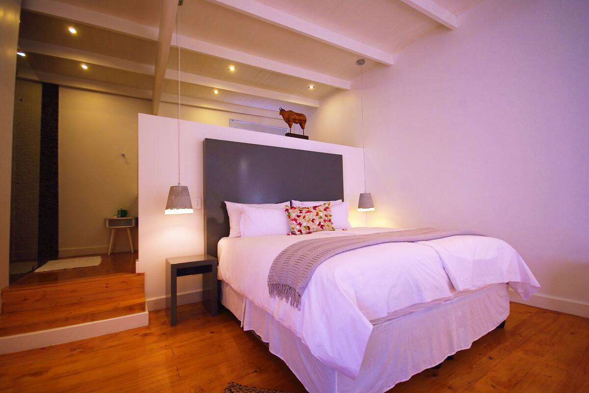 A modern bedroom with a large bed, a headboard, bedside lamps, and a small table.