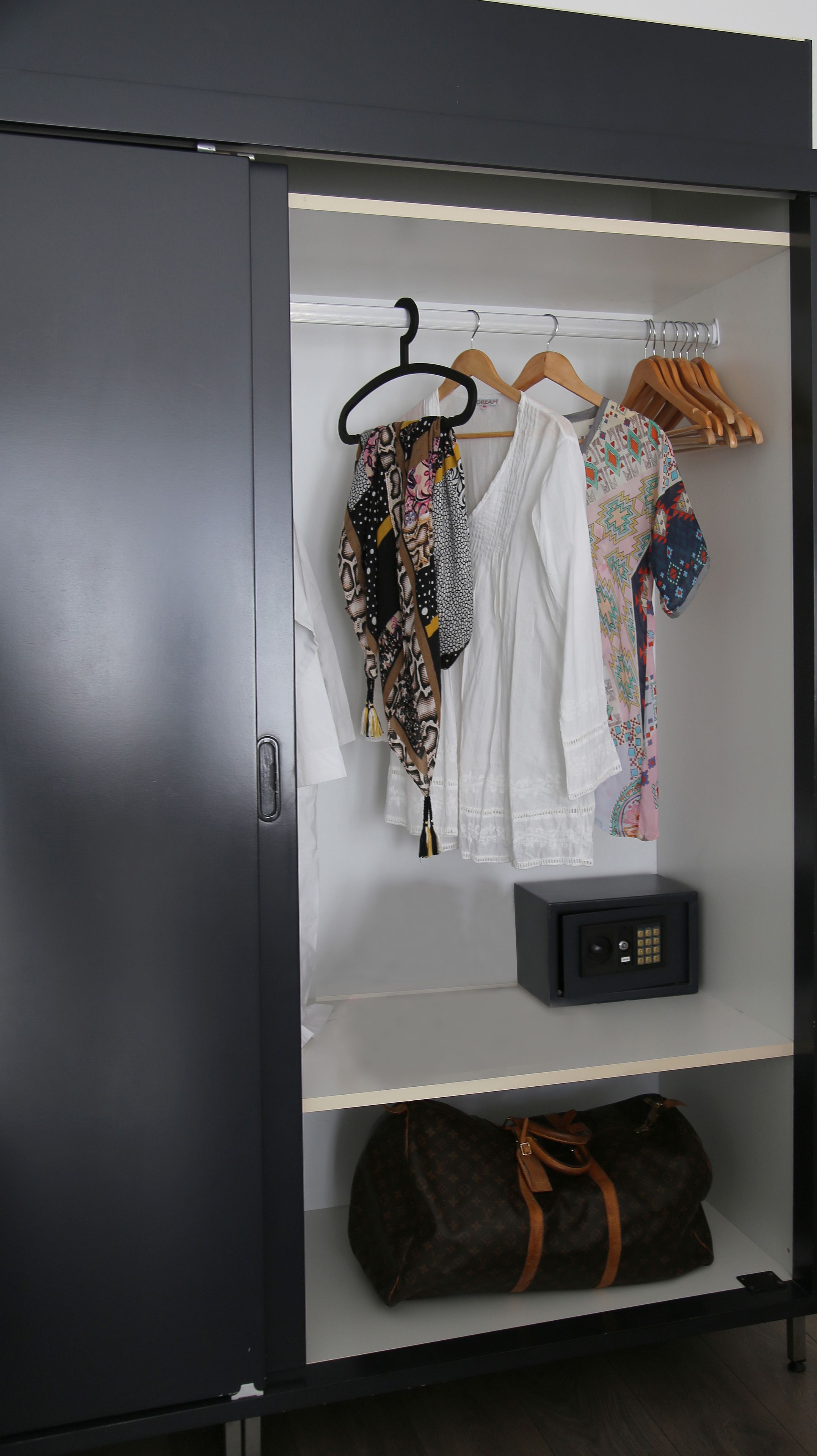 A wardrobe with hanging clothes, a safe, and a Louis Vuitton bag.