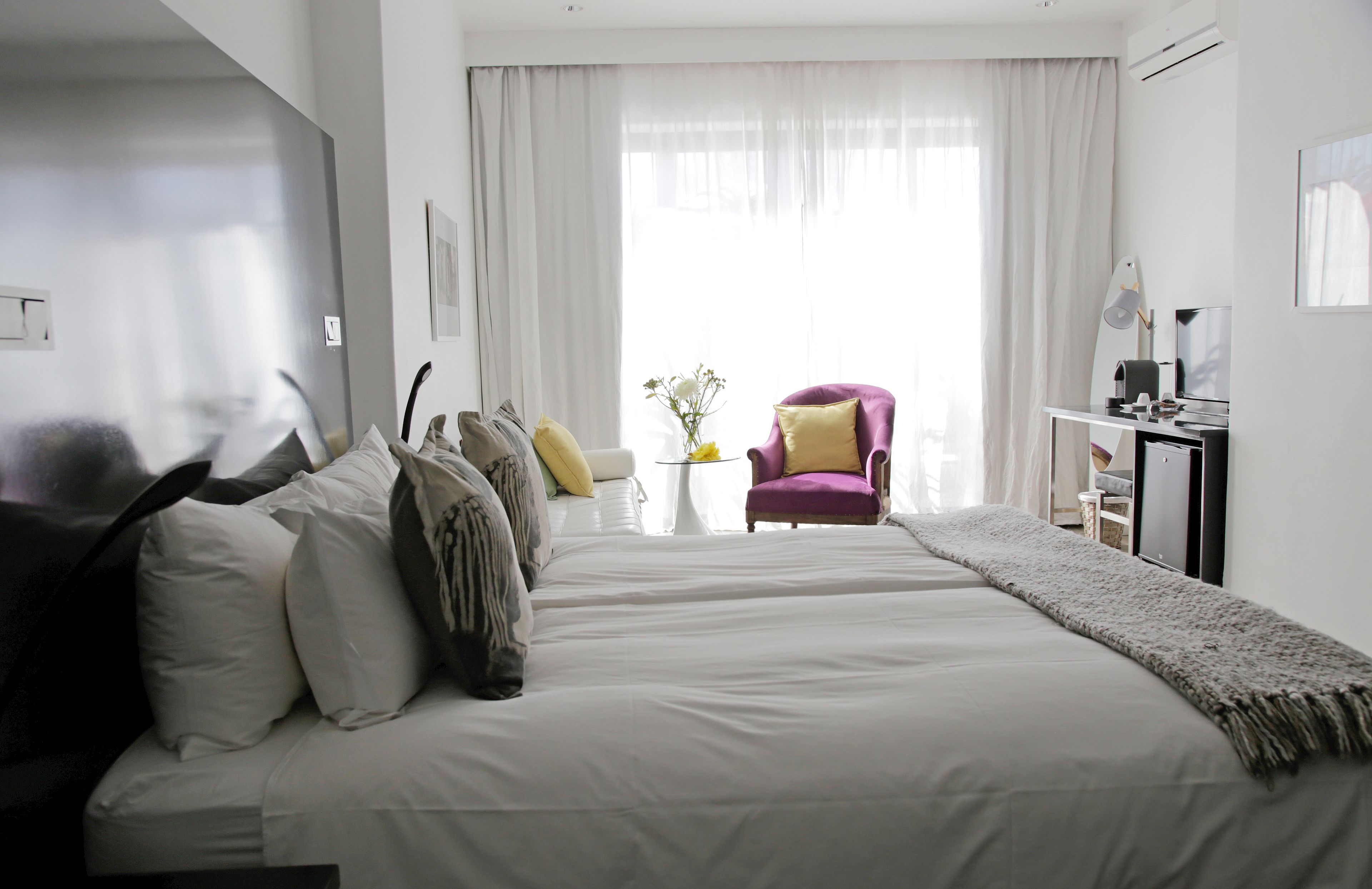 Ein modernes Hotelzimmer mit einem großen Bett, einem Schreibtisch mit Stuhl und Blick ins Freie durch transparente Vorhänge.
