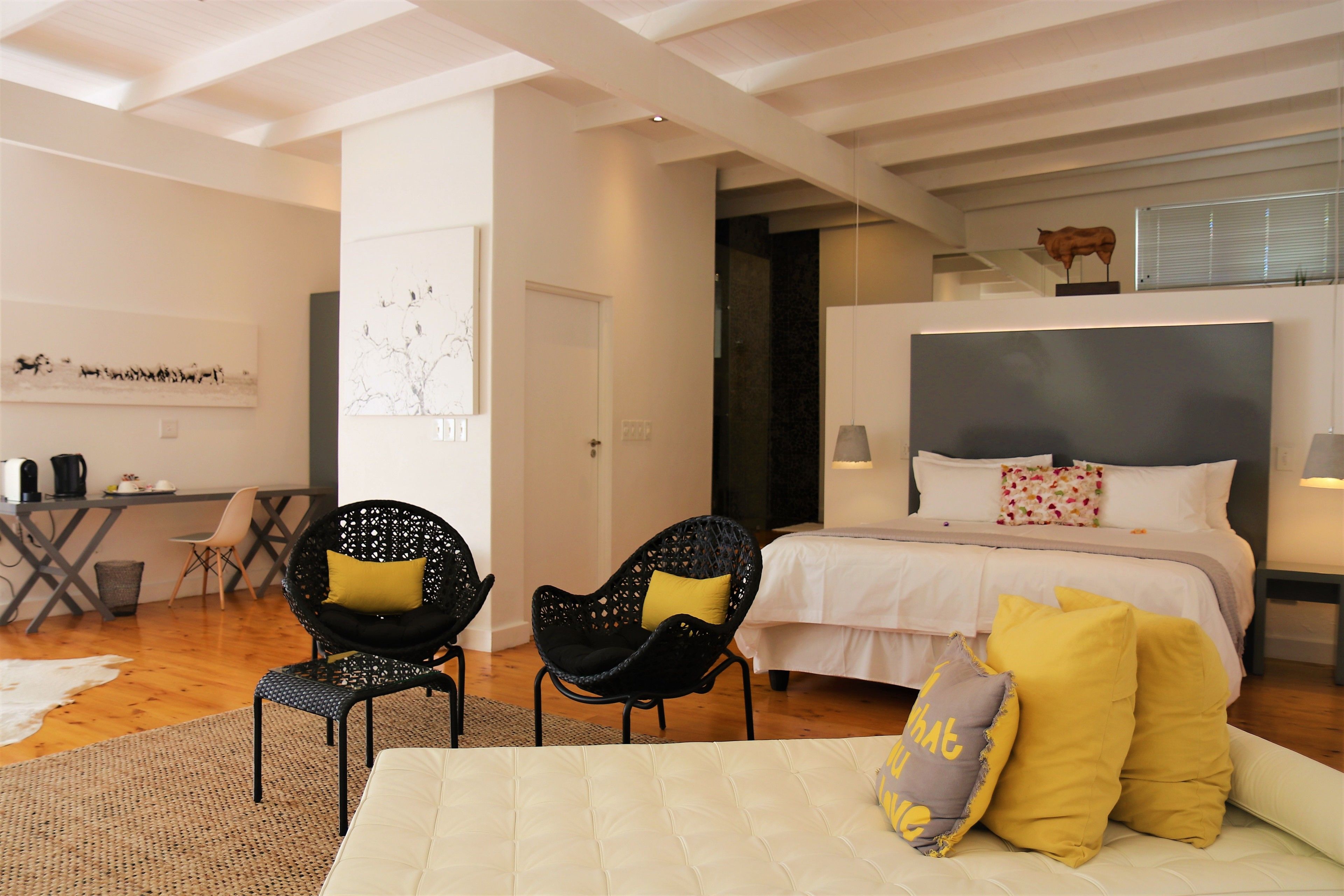 A modern bedroom with a large bed, two black chairs with yellow cushions, a white sofa, and a desk with a chair.