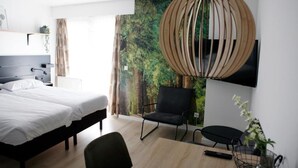 Een moderne hotelkamer met een bed, een bureau, een stoel en een groot muurschilderij.