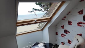 A room with a sloped ceiling, a view of the sea through a large window, a table with a picture, and a wall with a pattern of lips. - Le Regent & Spa (Pornichet)