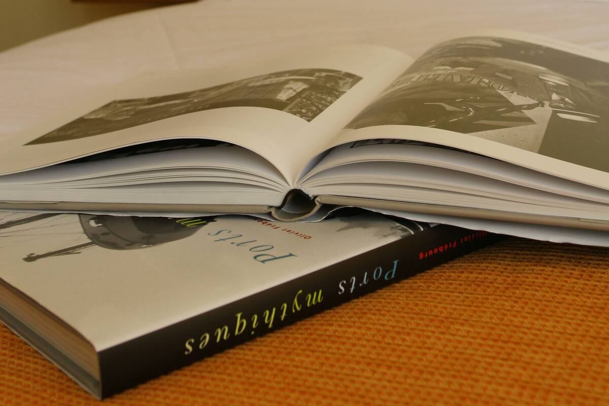An open book titled "Porsh" on a bed with white bedding, a lamp on a bedside table, and a yellow wall in the background.
