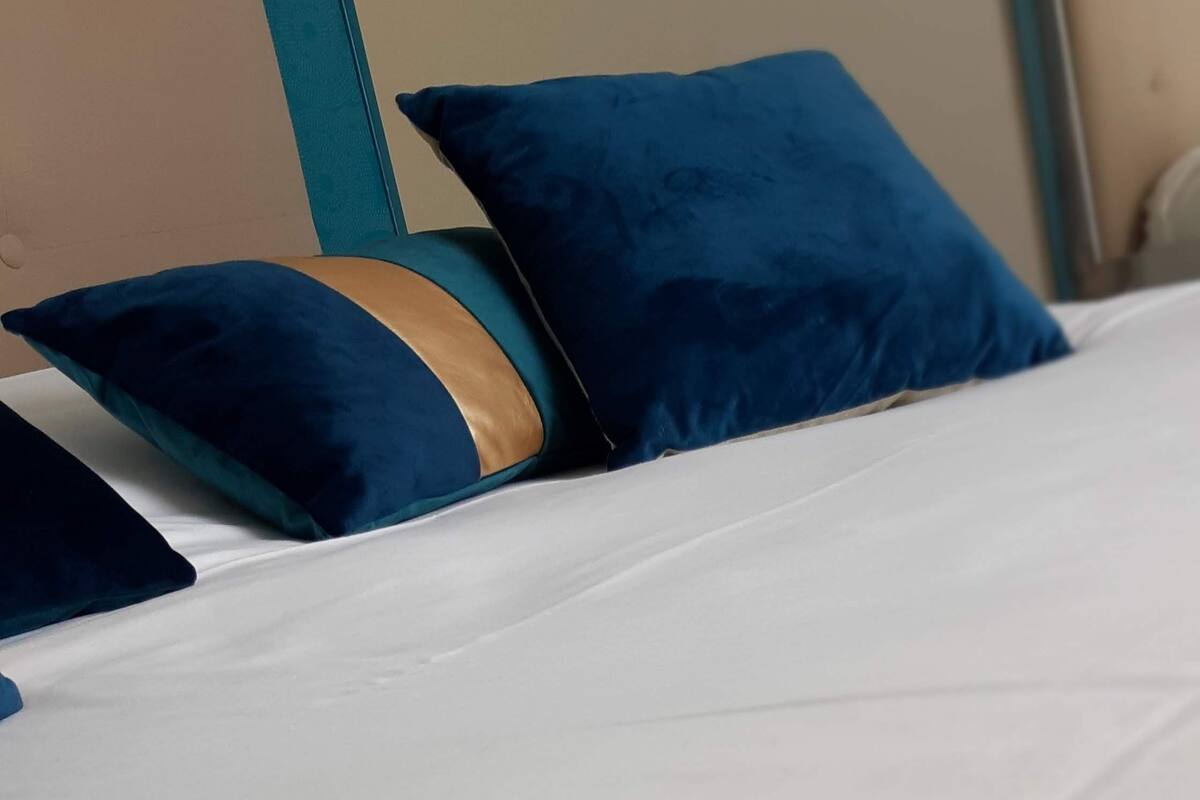 A bed with white bedding and two blue pillows.