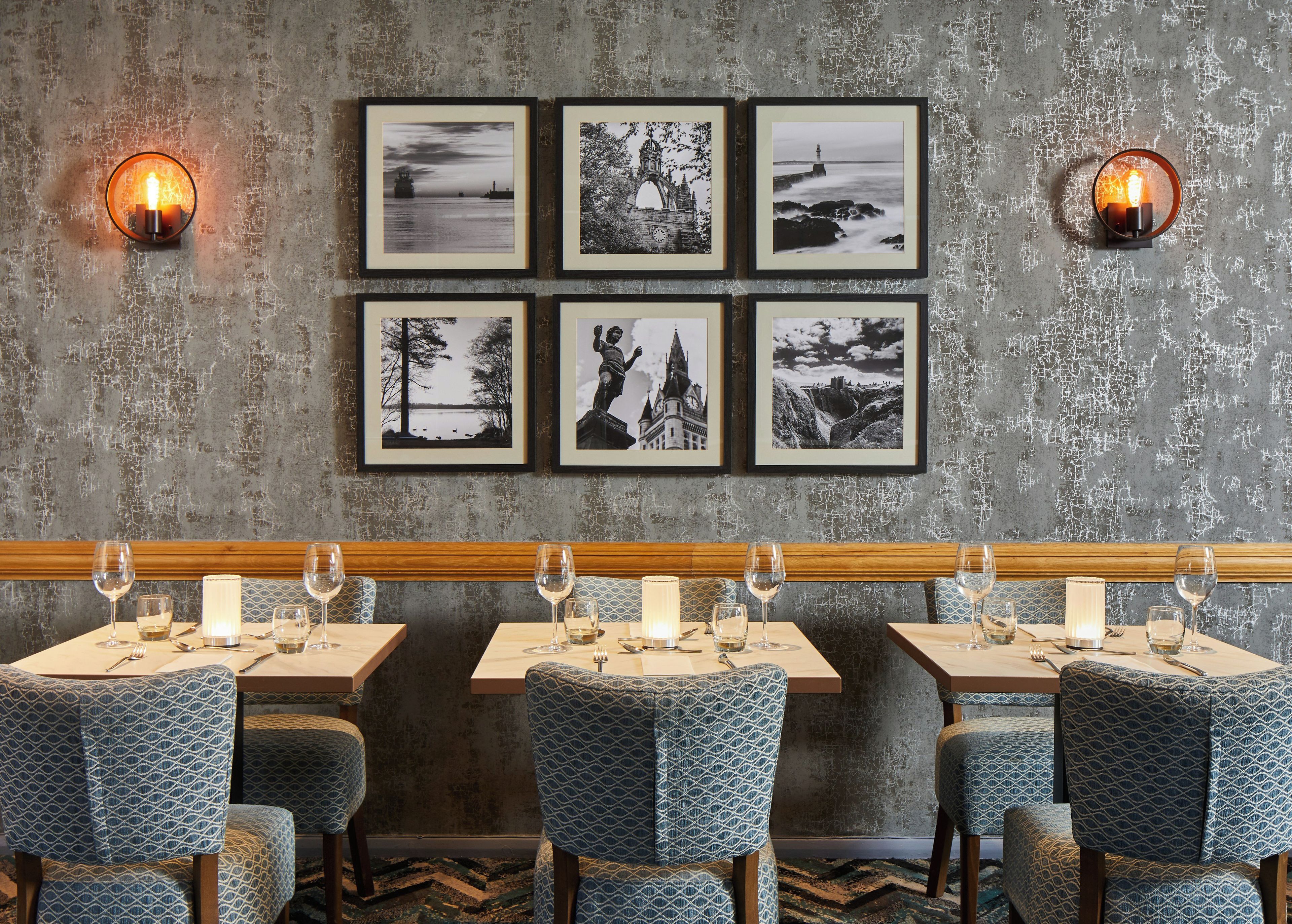 L’intérieur d’un restaurant présente un mur au style rustique, des photographies en noir et blanc encadrées et un long banc en bois.