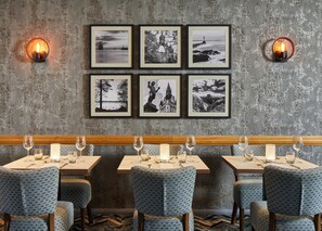A restaurant interior with a rustic wall, framed black and white photographs, and a long wooden bench.