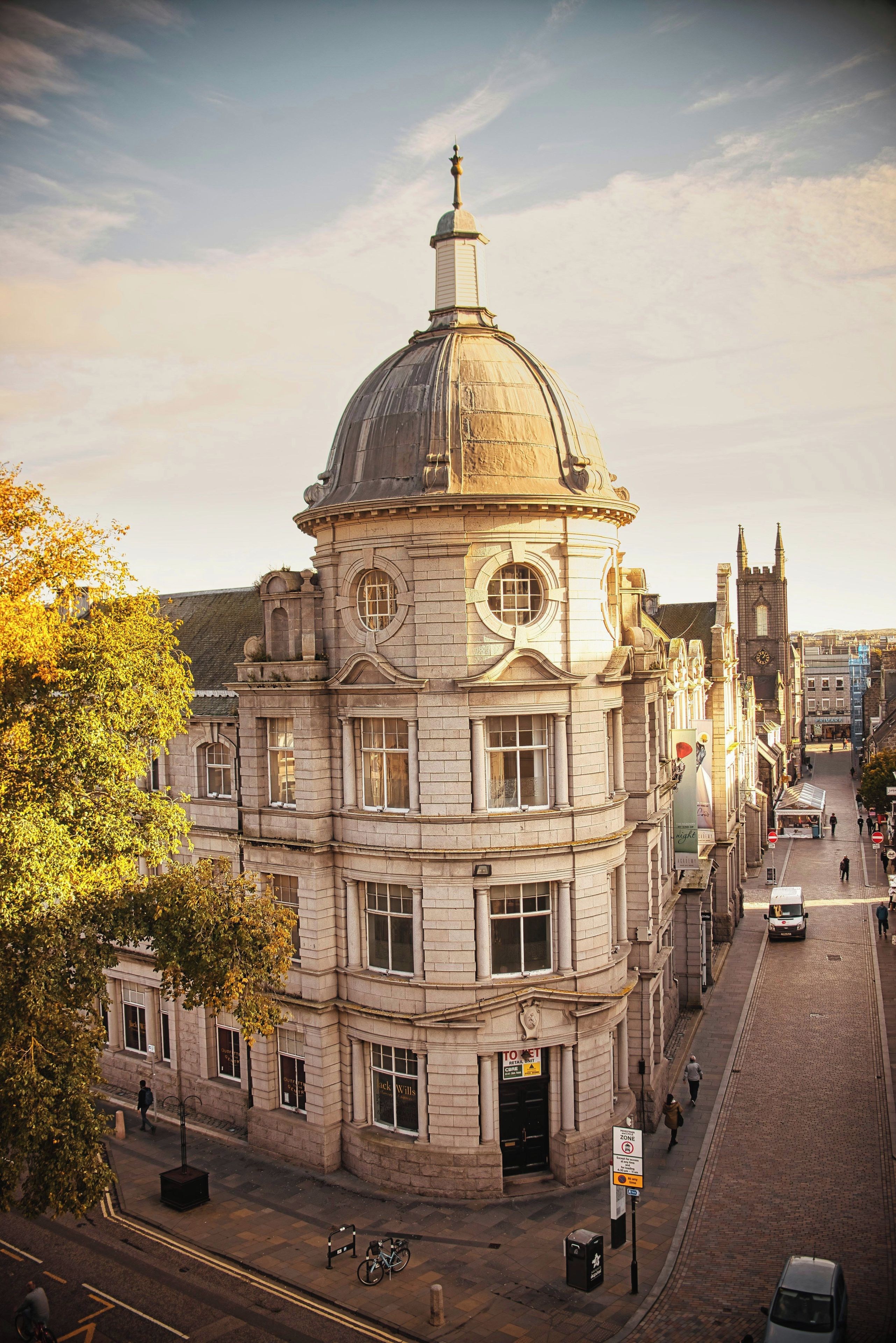 A historic building with a prominent dome and arched windows, situated on a city street with a clear sky.