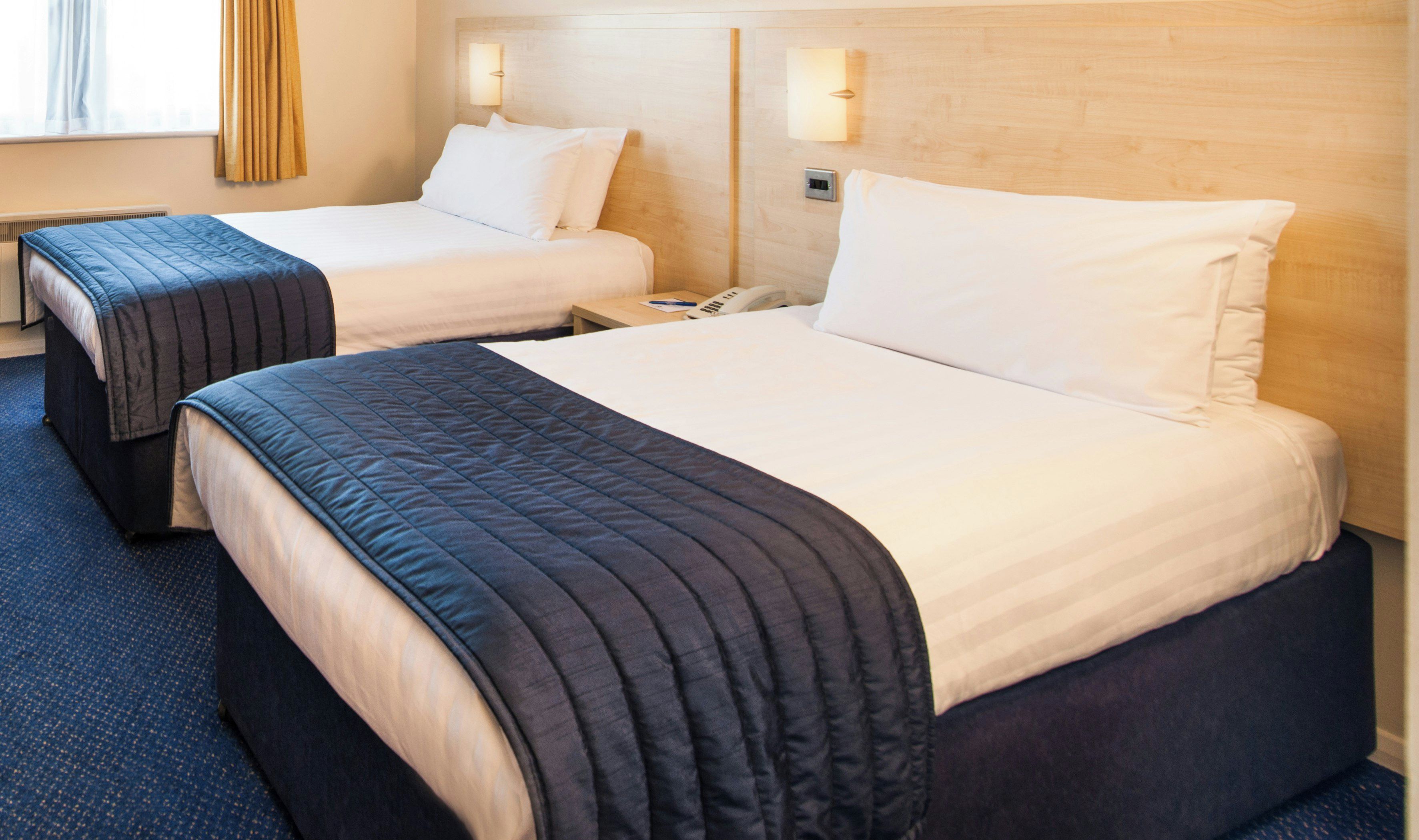 Two double beds with headboards, a bedside table with a phone, and a wall-mounted light fixture.