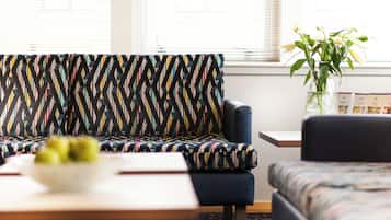 A modern living room with a patterned sofa, a small table with a bowl of fruit, and a vase with flowers.