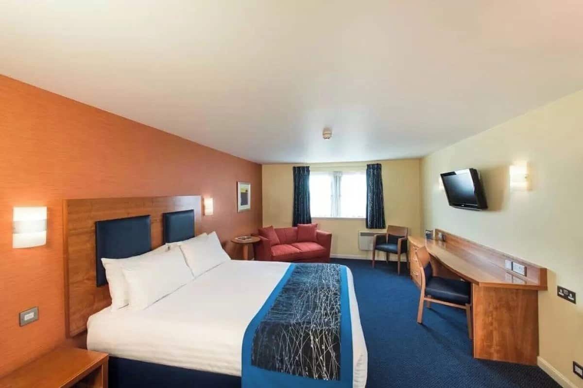 A hotel room with a large bed, a desk, a chair, a television, and a window with curtains.