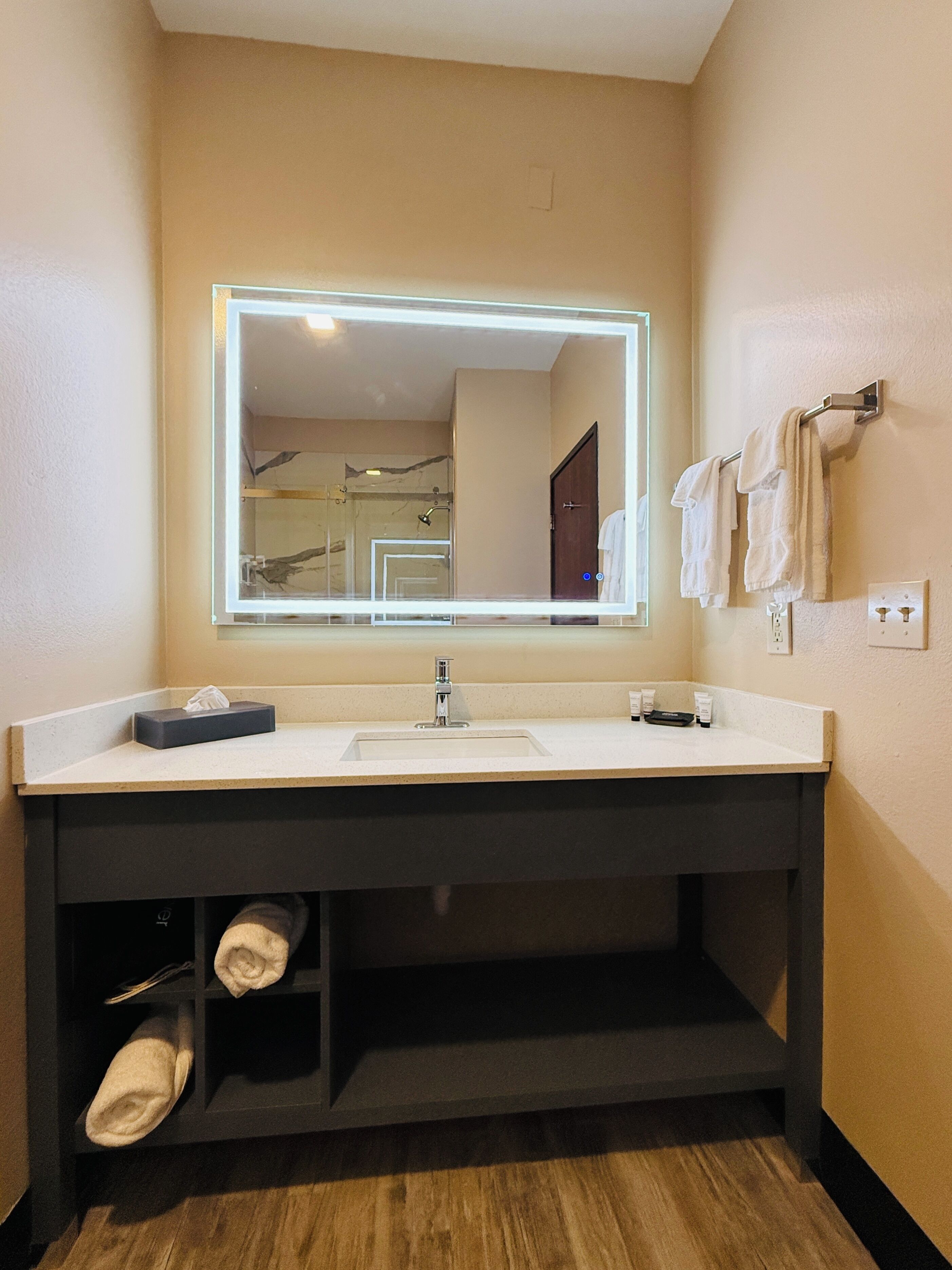 A bathroom with a large mirror, a sink, and a towel rack.