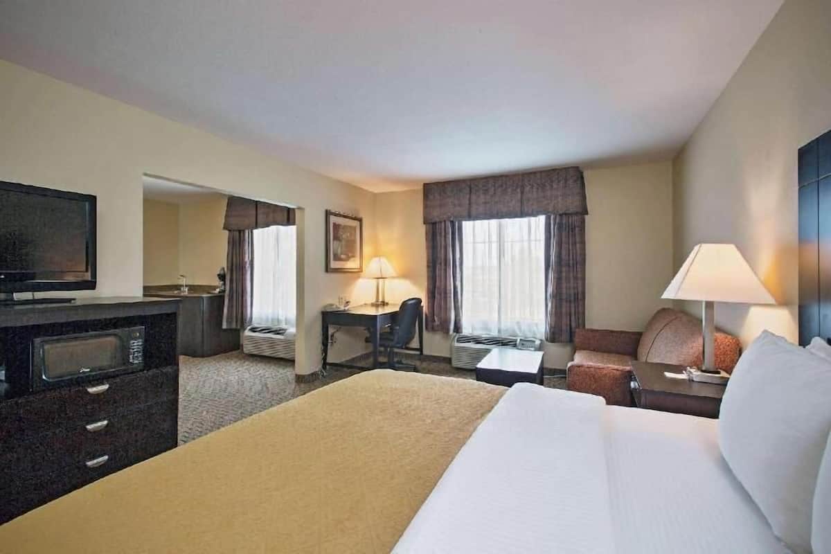 Een hotelkamer met een bed, een bureau, een stoel, een televisie, een lamp en een raam met gordijnen.