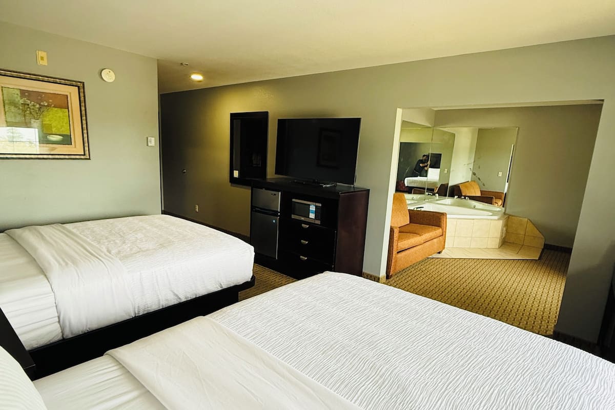 Een hotelkamer met twee bedden, een televisie, een dressoir, en een badkamer zichtbaar door een geopende deur.