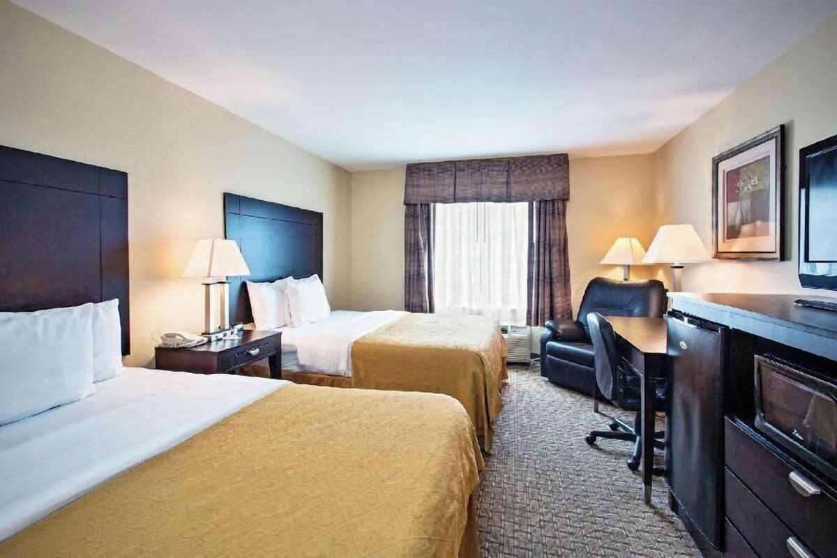 Een hotelkamer met twee bedden, een bureau, een stoel, een televisie en een raam met gordijnen.