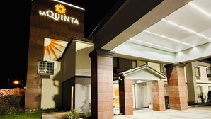 L’entrée d’un hôtel, avec une enseigne indiquant « LA QUINTA », un espace extérieur abrité et la façade du bâtiment.