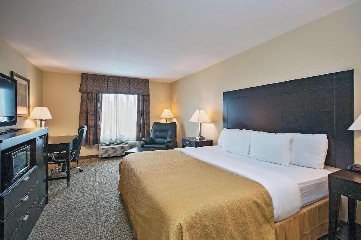 Een hotelkamer met een bed, twee nachtkastjes, een bureau met stoel, een televisie en een raam met gordijnen.