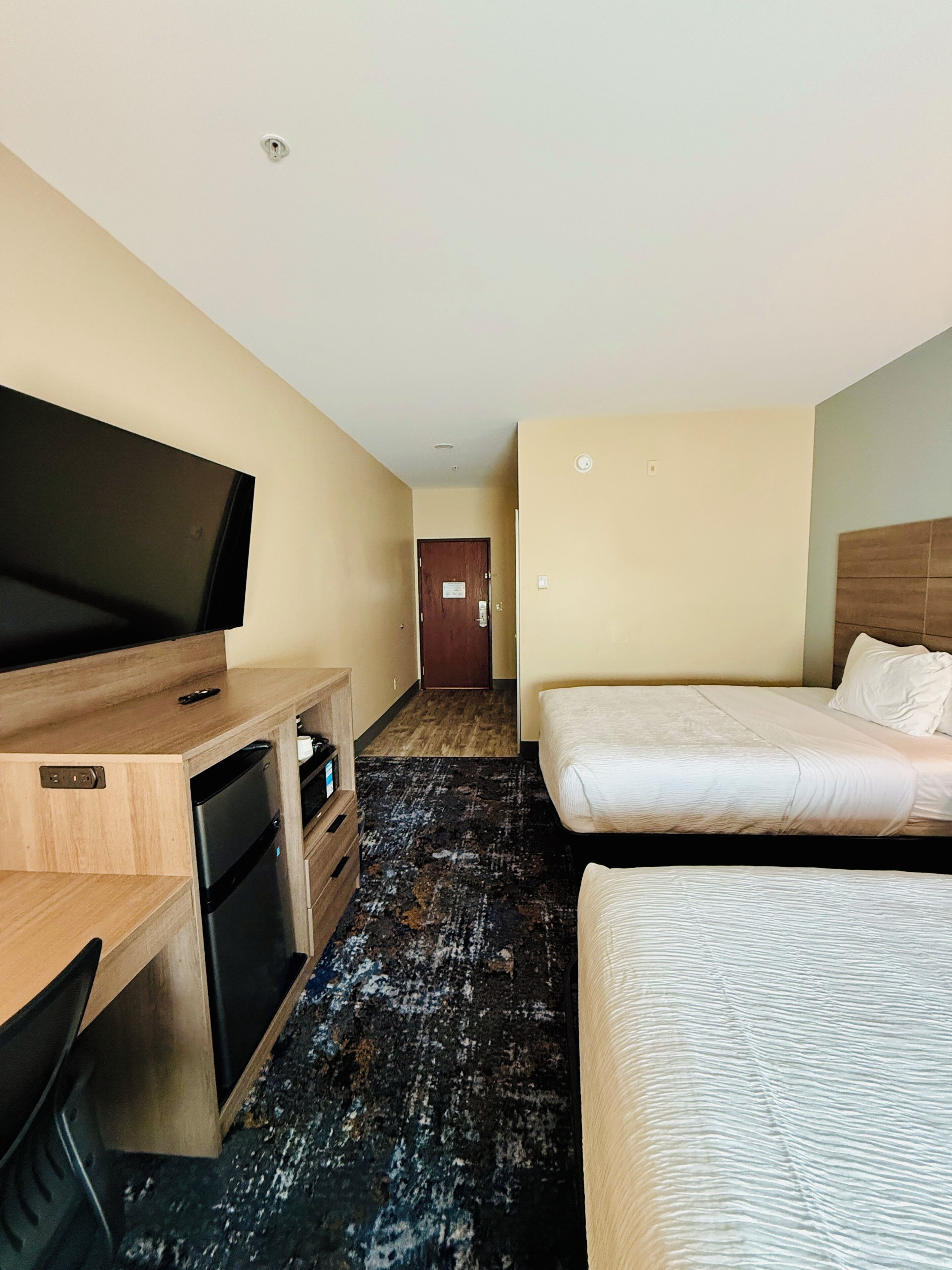 A hotel room with a bed, a TV, a desk with a computer, and a small kitchenette.
