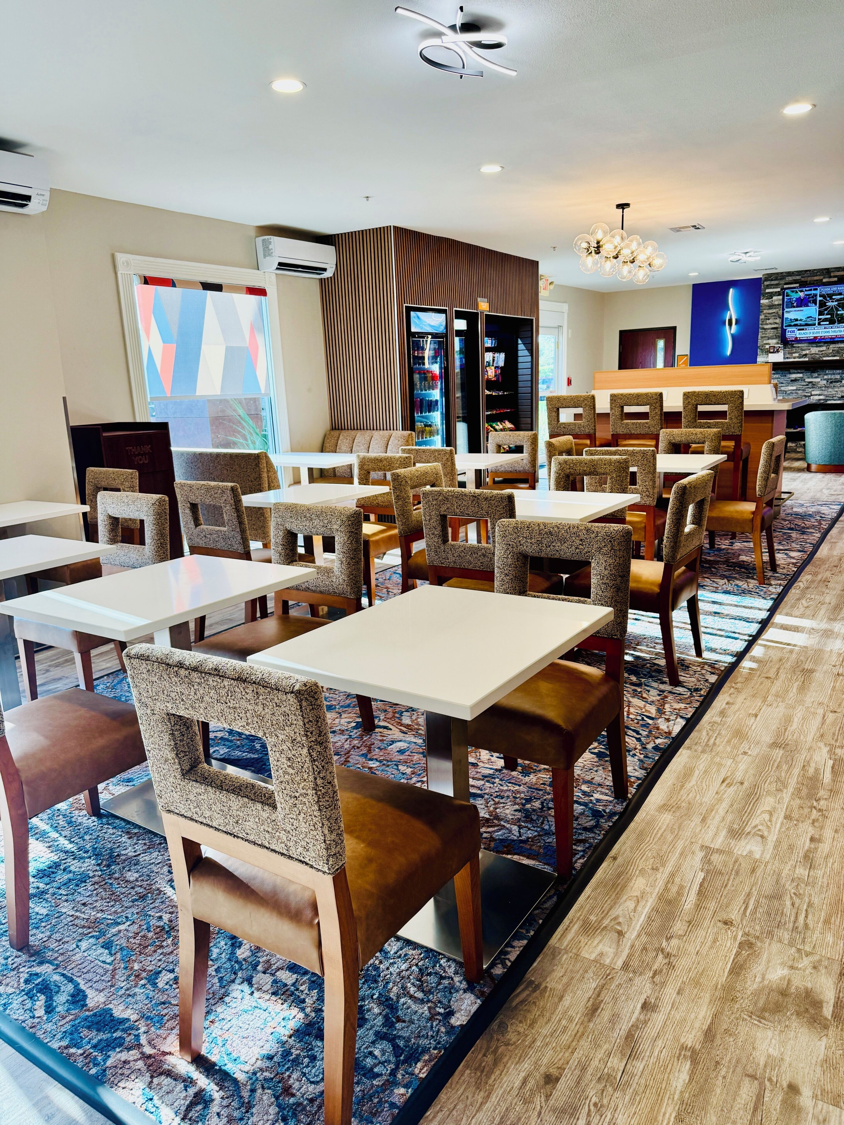 En restaurant i et hotel med flere borde og stole, et mønstret tæppe og et moderne loftdesign.