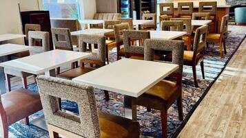 En restaurant i et hotel med flere borde og stole, et mønstret tæppe og et moderne loftdesign.