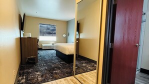 Une chambre d’hôtel avec un lit, un miroir, une télévision et une fenêtre ornée d’un motif géométrique.