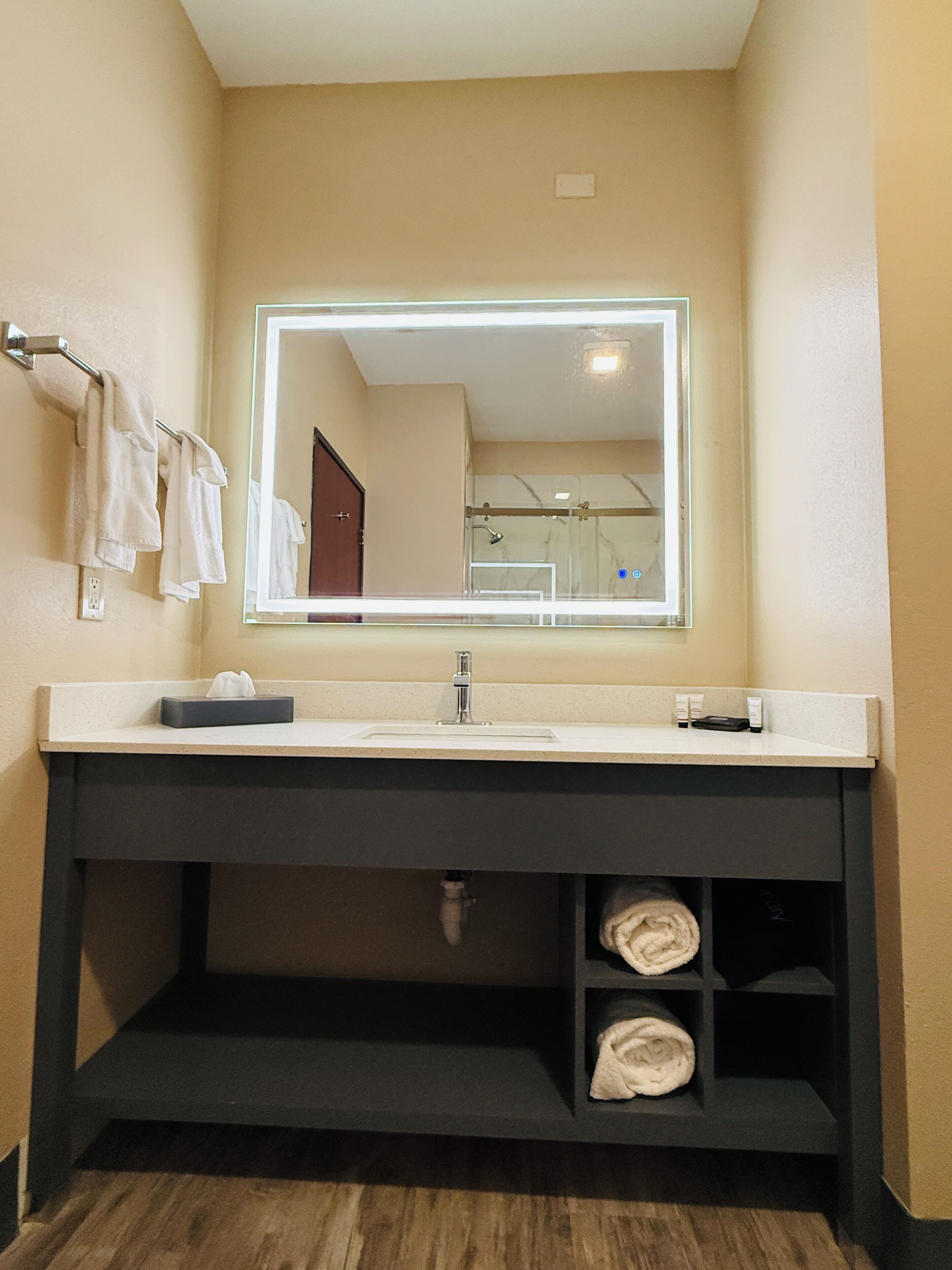 A bathroom with a large mirror, a sink, a towel rack, and a shelf with towels.