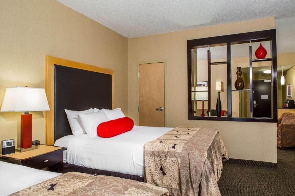 Habitación de hotel con cama, mesita de noche, lámpara y un espejo grande.