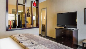 Ein Hotelzimmer mit Bett, Kommode, Fernseher und einem großen Spiegel.