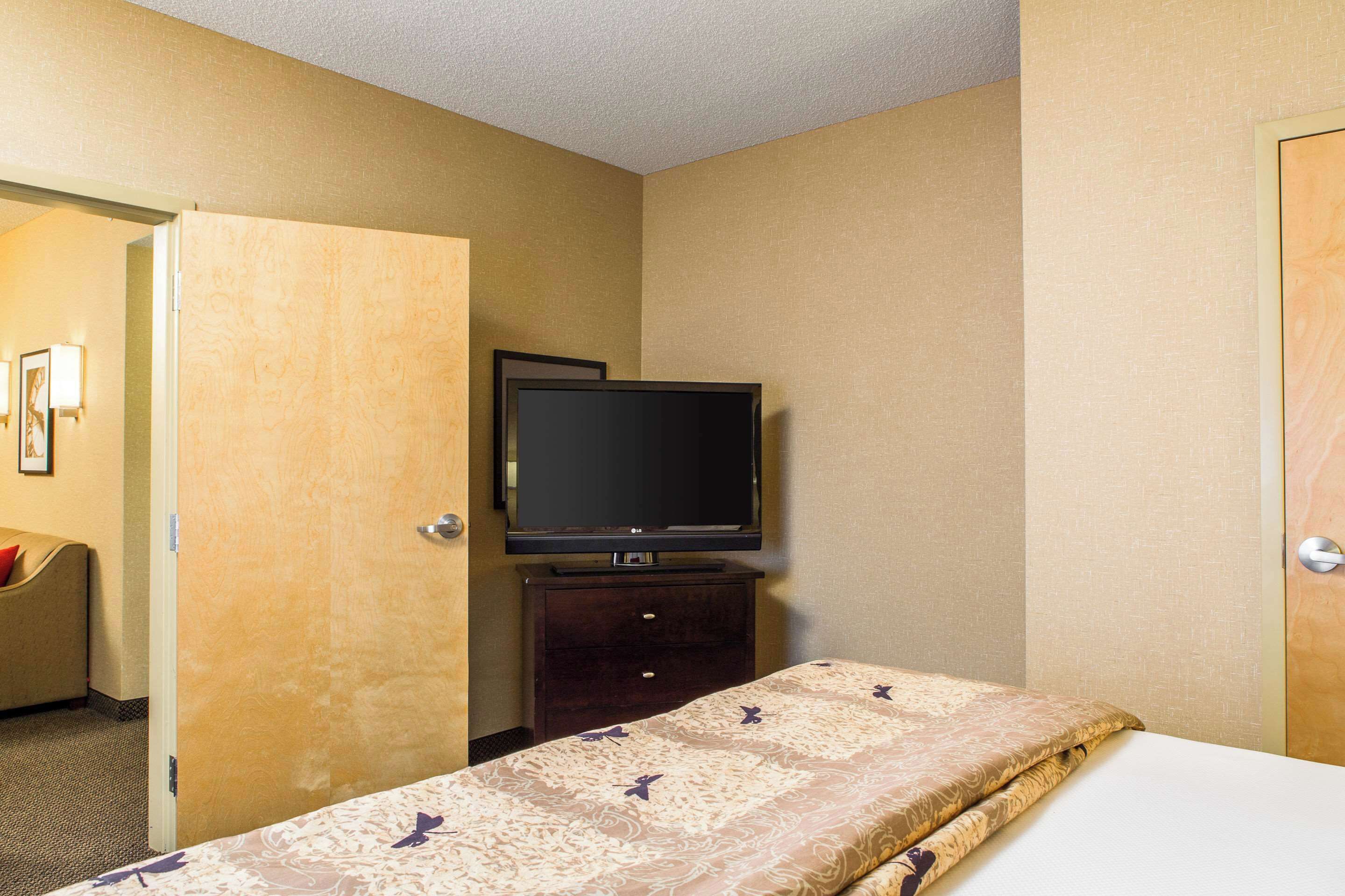 Una habitación de hotel con una cama, un televisor sobre un soporte y una puerta que da a otra habitación.