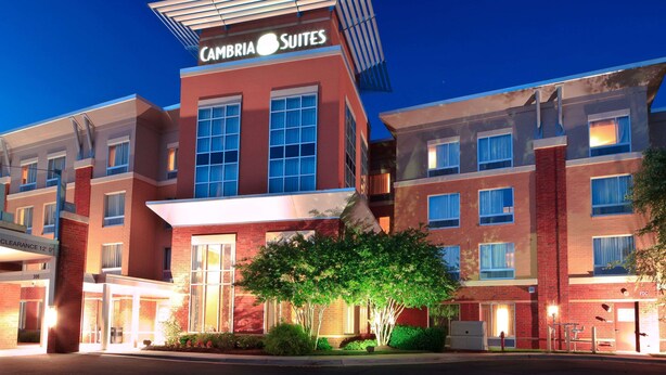 Ein mehrstöckiges Hotel mit einem gut sichtbaren 'Cambria Suites'-Schild, großen Fenstern und einem überdachten Eingangsbereich.