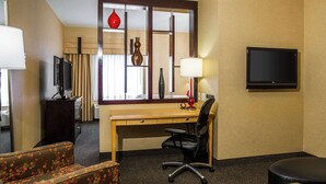 Ein Hotelzimmer mit Schreibtisch, Stuhl, Fernseher, Lampe und einem Fenster mit Vorhängen.