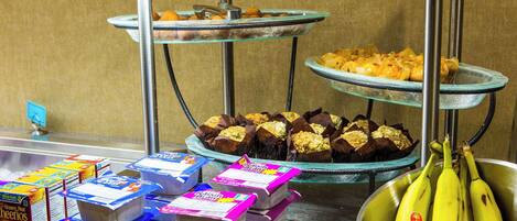 A buffet with various food items including pastries, boxed food, and bananas.