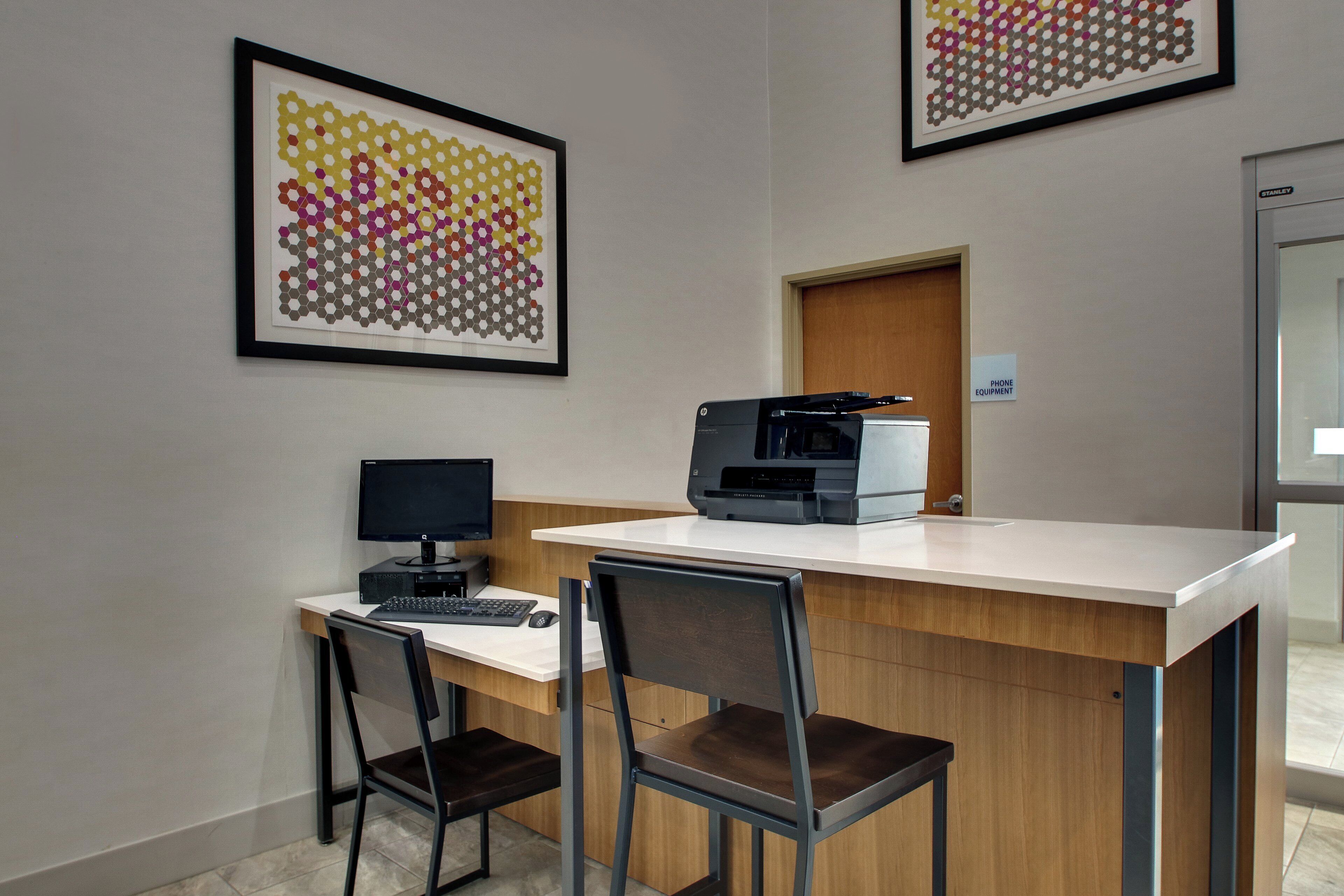 A reception desk with a computer, two chairs, and a printer. There are framed artworks on the wall.