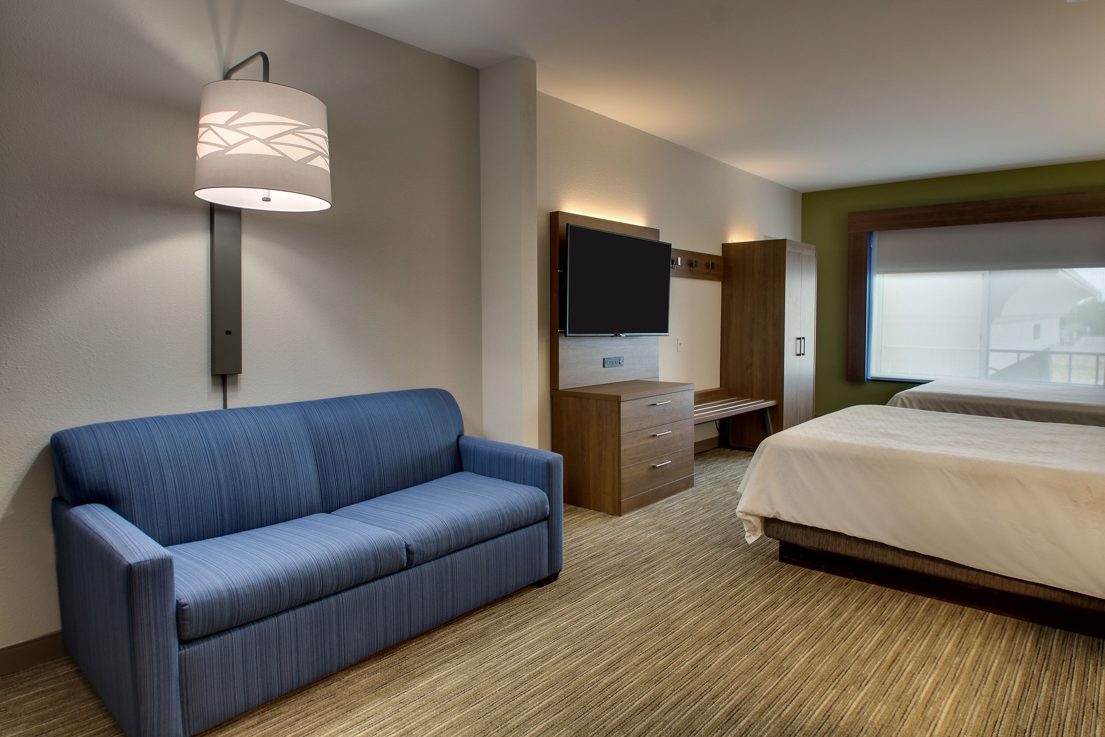 A hotel room with a sofa, a bed, a flat-screen TV, a dresser, and a large window.