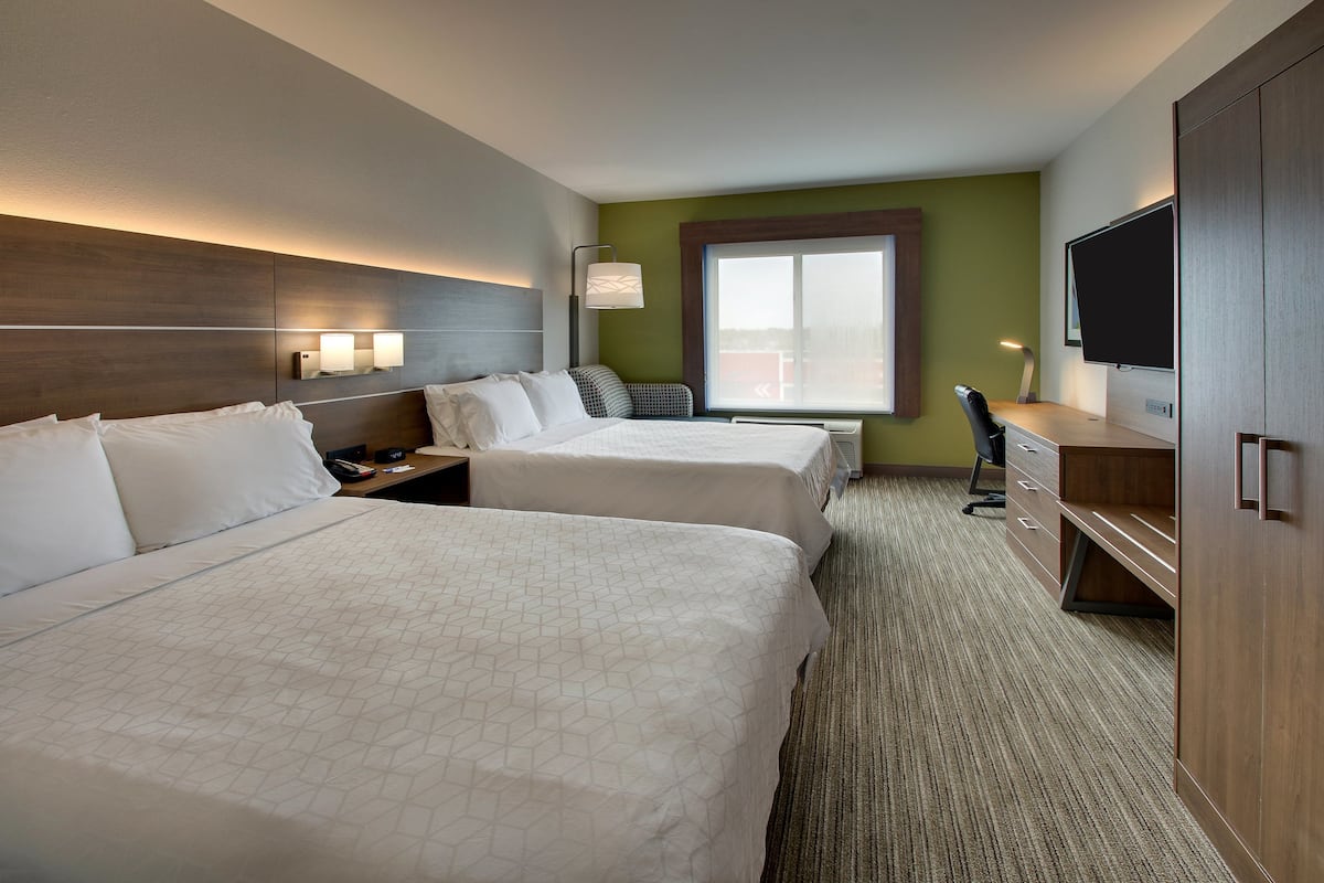 A hotel room with two beds, a desk, a chair, a TV, and a window.