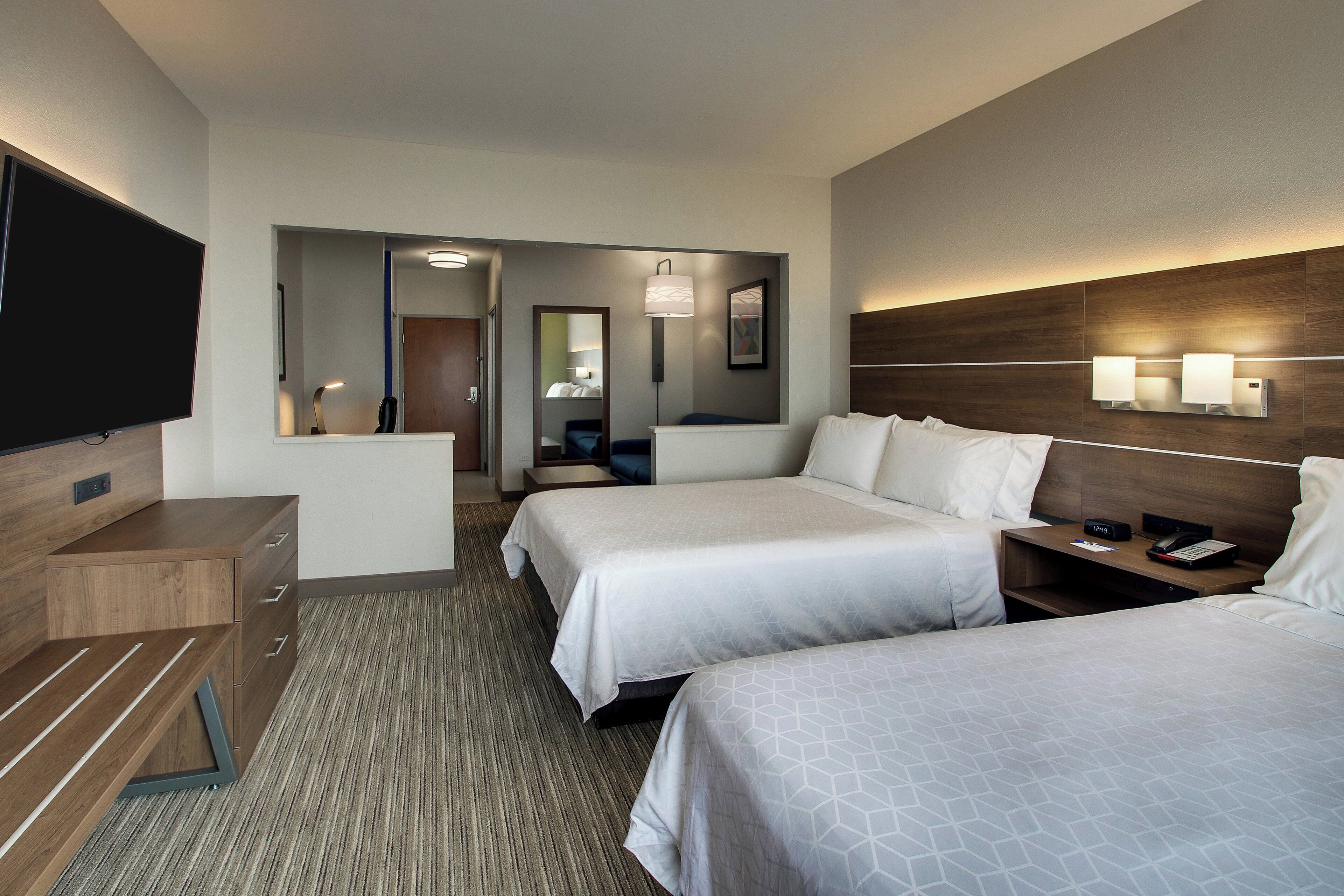 Une chambre d’hôtel avec deux lits, un bureau, une télévision et une salle de bain visible à travers une porte ouverte.