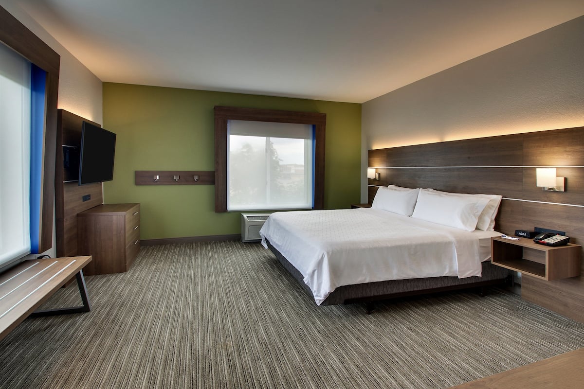 A hotel room with a bed, bedside tables, a TV, and a window.