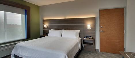 A hotel room with a large bed, a nightstand, a wooden door, and a window.