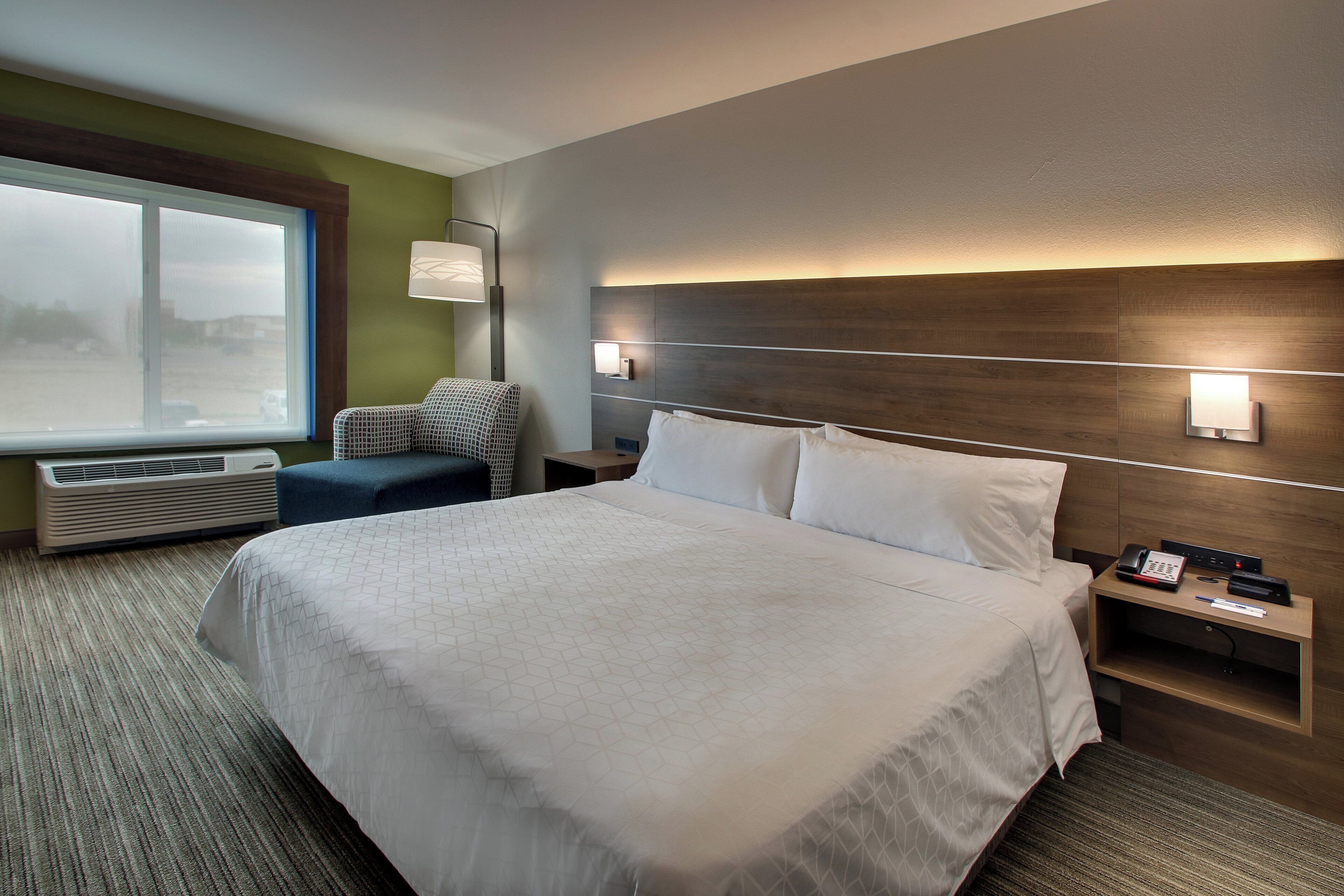Habitación de hotel con una cama grande, un escritorio con teléfono y lámpara, una ventana con vista al exterior y un aplique de pared.