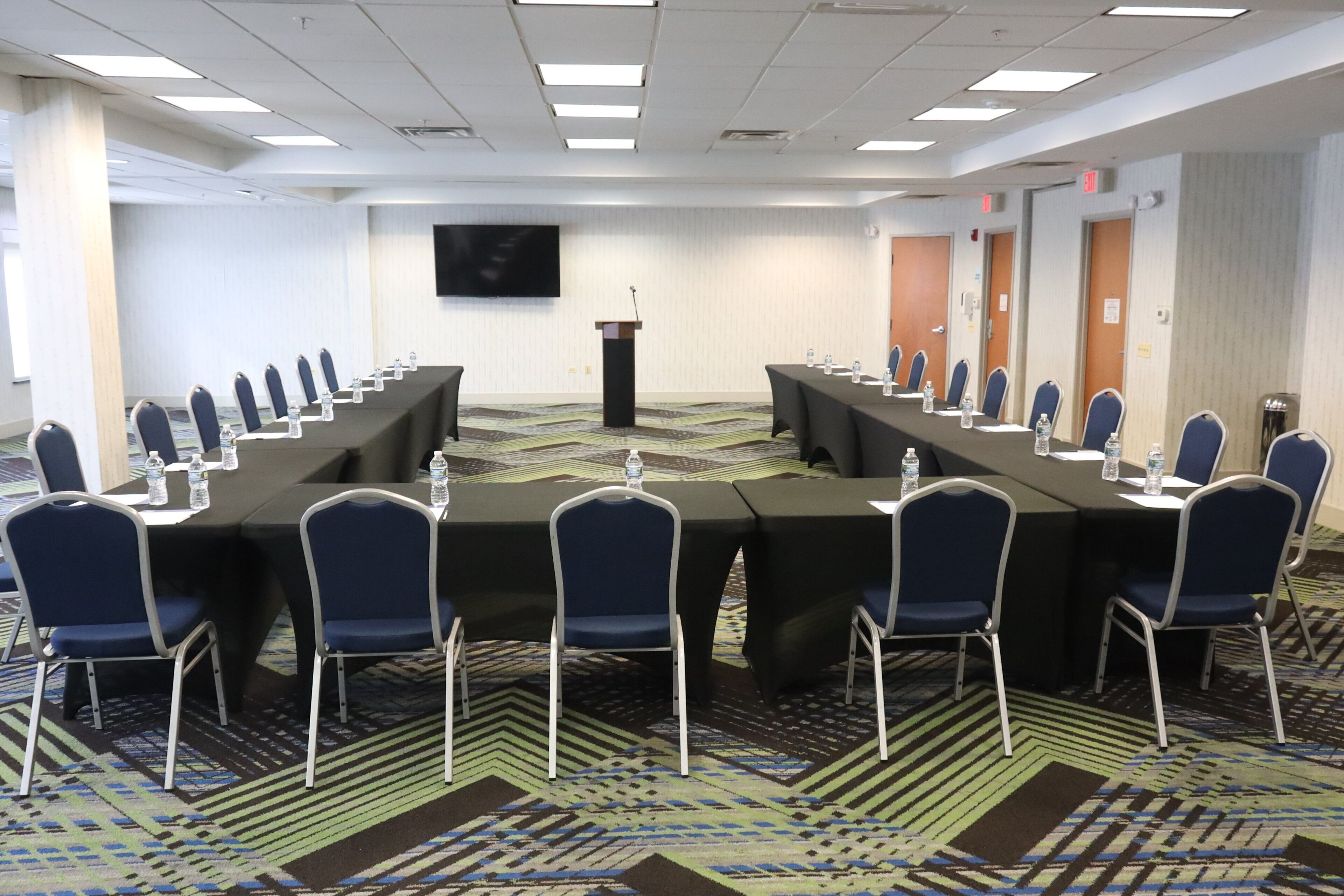 A conference room with a long table, chairs, a podium, and a flat-screen TV on the wall.