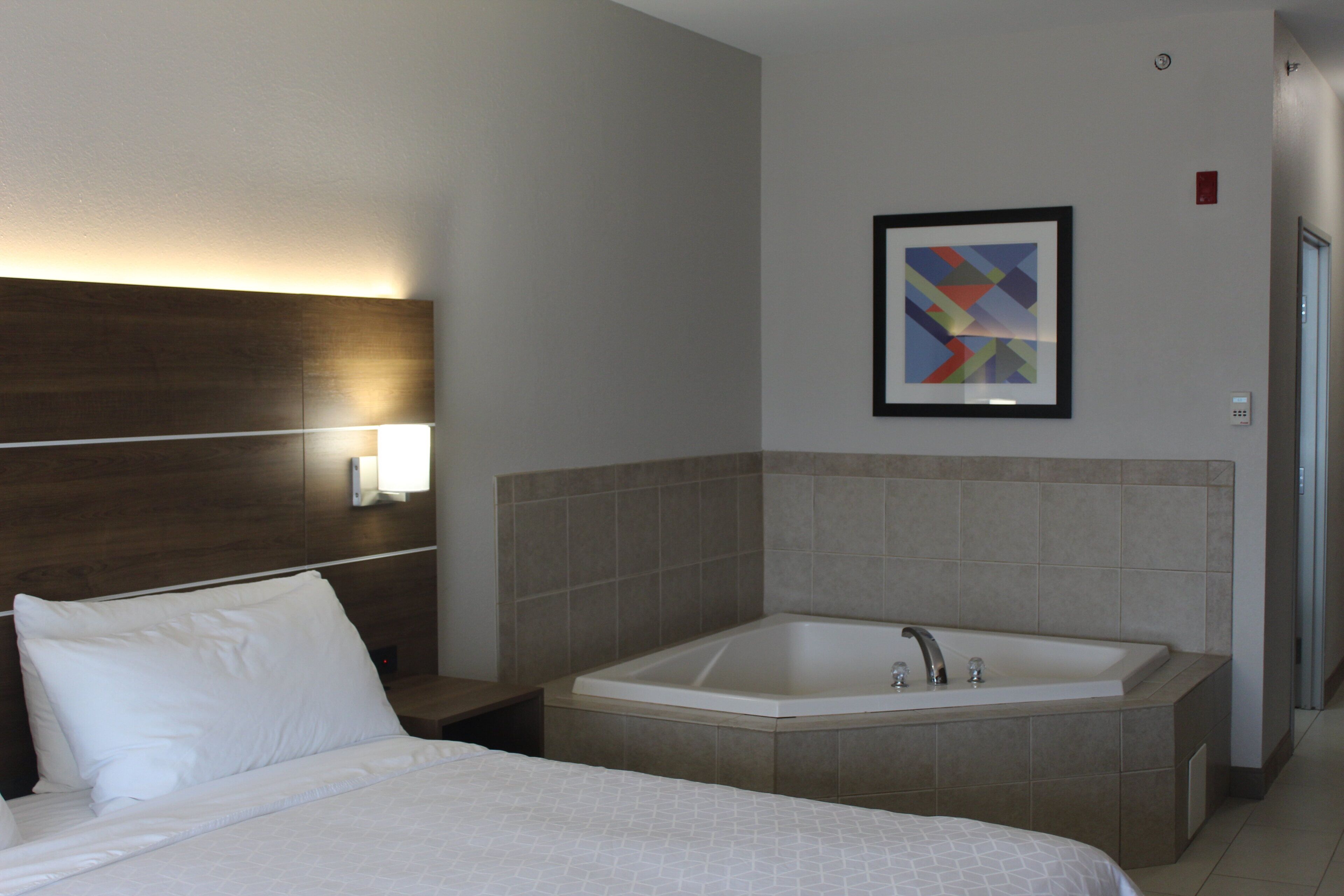 A hotel room with a bed, a large bathtub, and a wall-mounted light fixture.