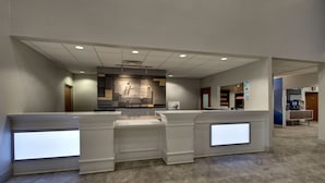 Un espace d’accueil d’hôtel au design moderne, comprenant un comptoir d’accueil, un écran numérique et un coin salon.