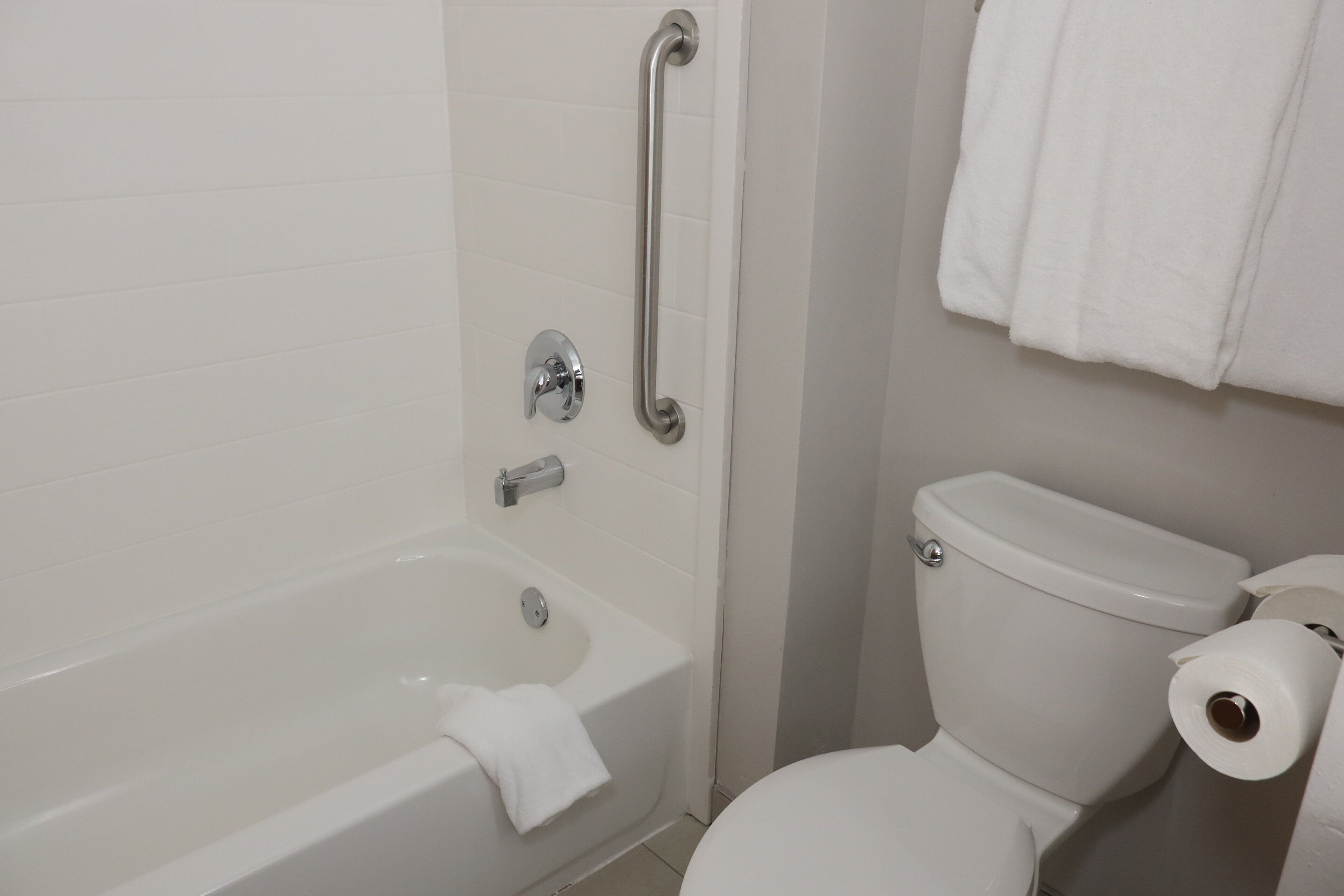 A bathroom with a bathtub, toilet, and a handrail.