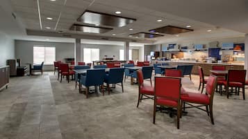 Un grand espace dédié à la salle à manger, avec de nombreuses tables et chaises, un comptoir où sont exposés les plats, et de grandes fenêtres qui laissent entrer la lumière naturelle.