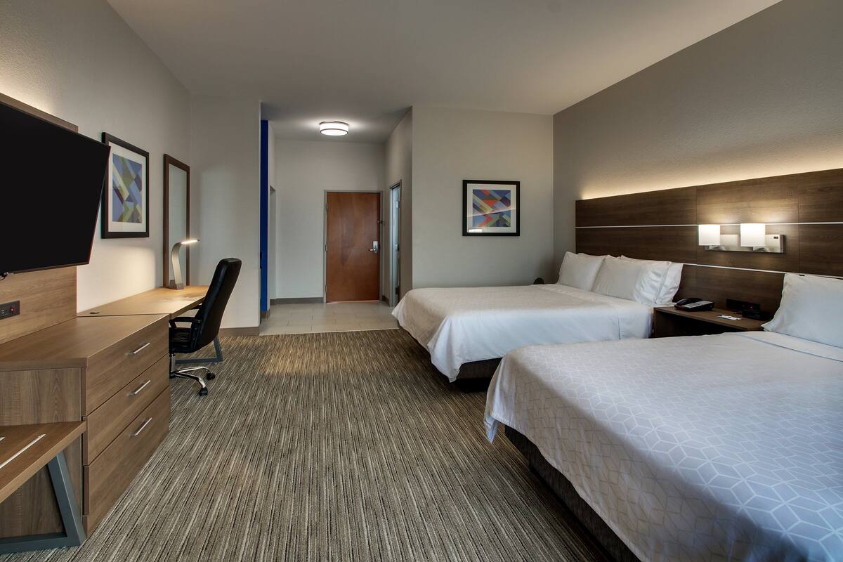 A hotel room with two beds, a desk, a chair, a TV, and artwork on the walls.