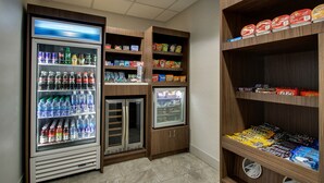 Un espace de libre-service où l’on peut se servir des boissons et des en-cas, avec des distributeurs de boissons réfrigérés, des étagères remplies d’en-cas et un congélateur.